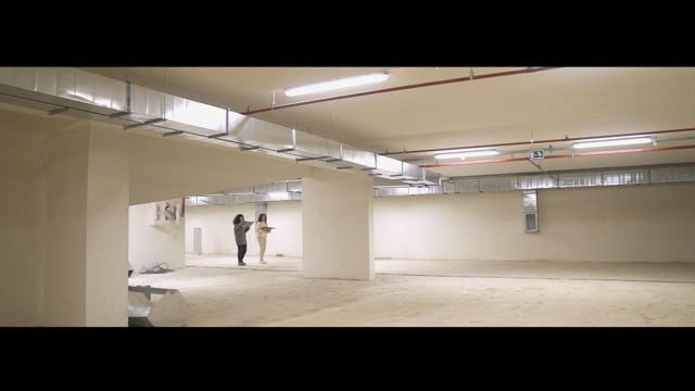 The empty car park, two figures far off, still from the video