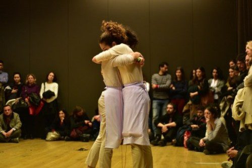 Two performers embracing in front of a seated audience