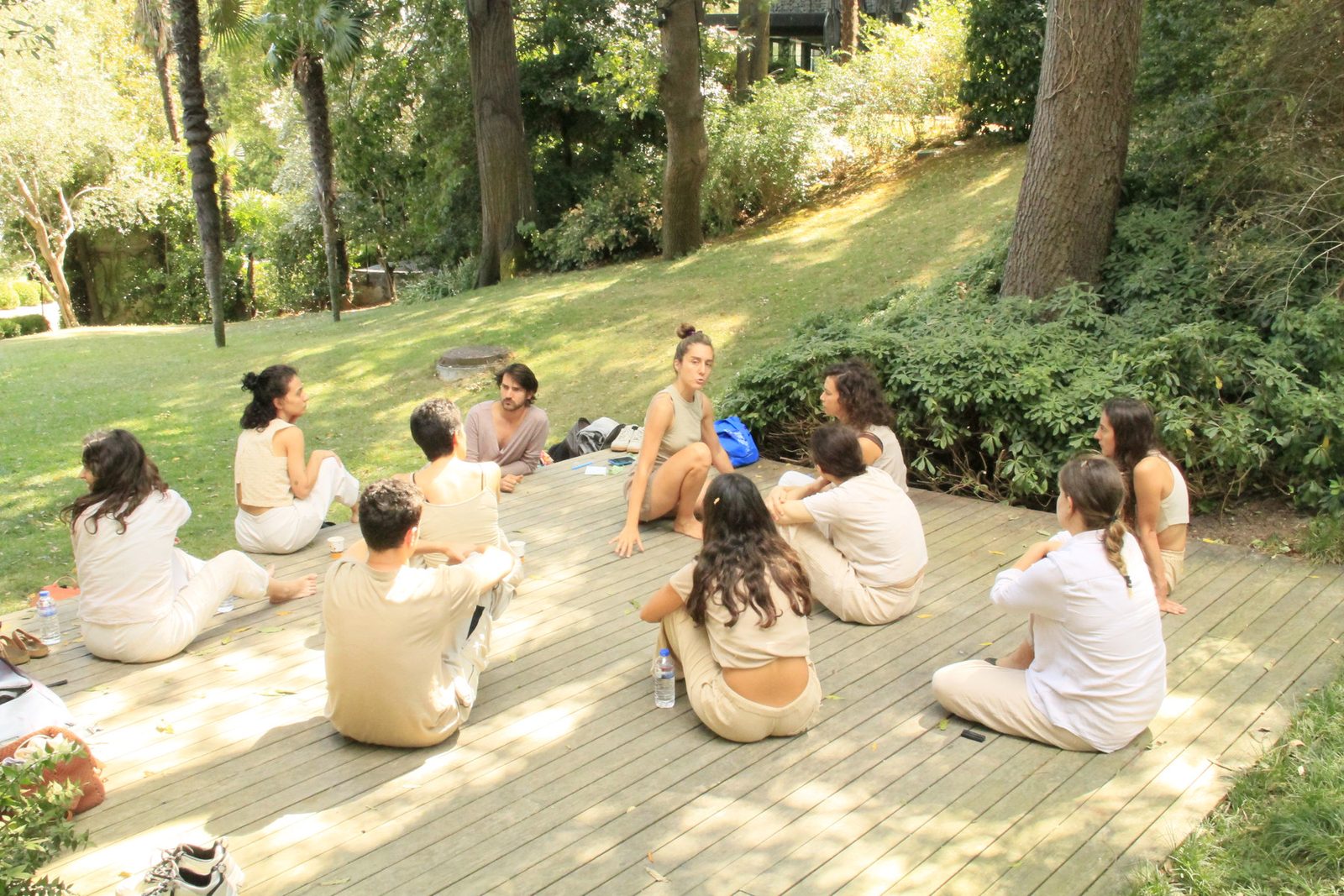 Participants seated in a circle on a wooden deck under the trees