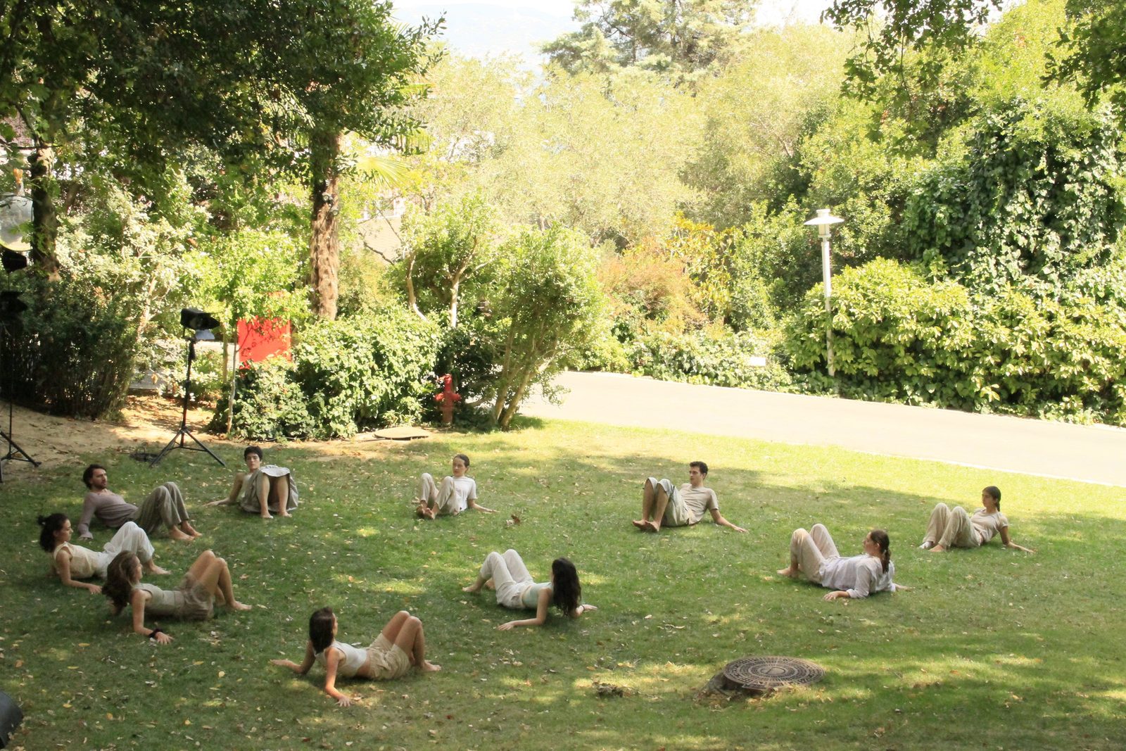Performers lying scattered across a sunlit lawn