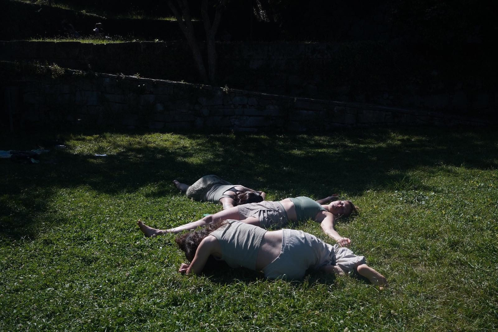 A performer crawling across the grass towards another lying in the shade