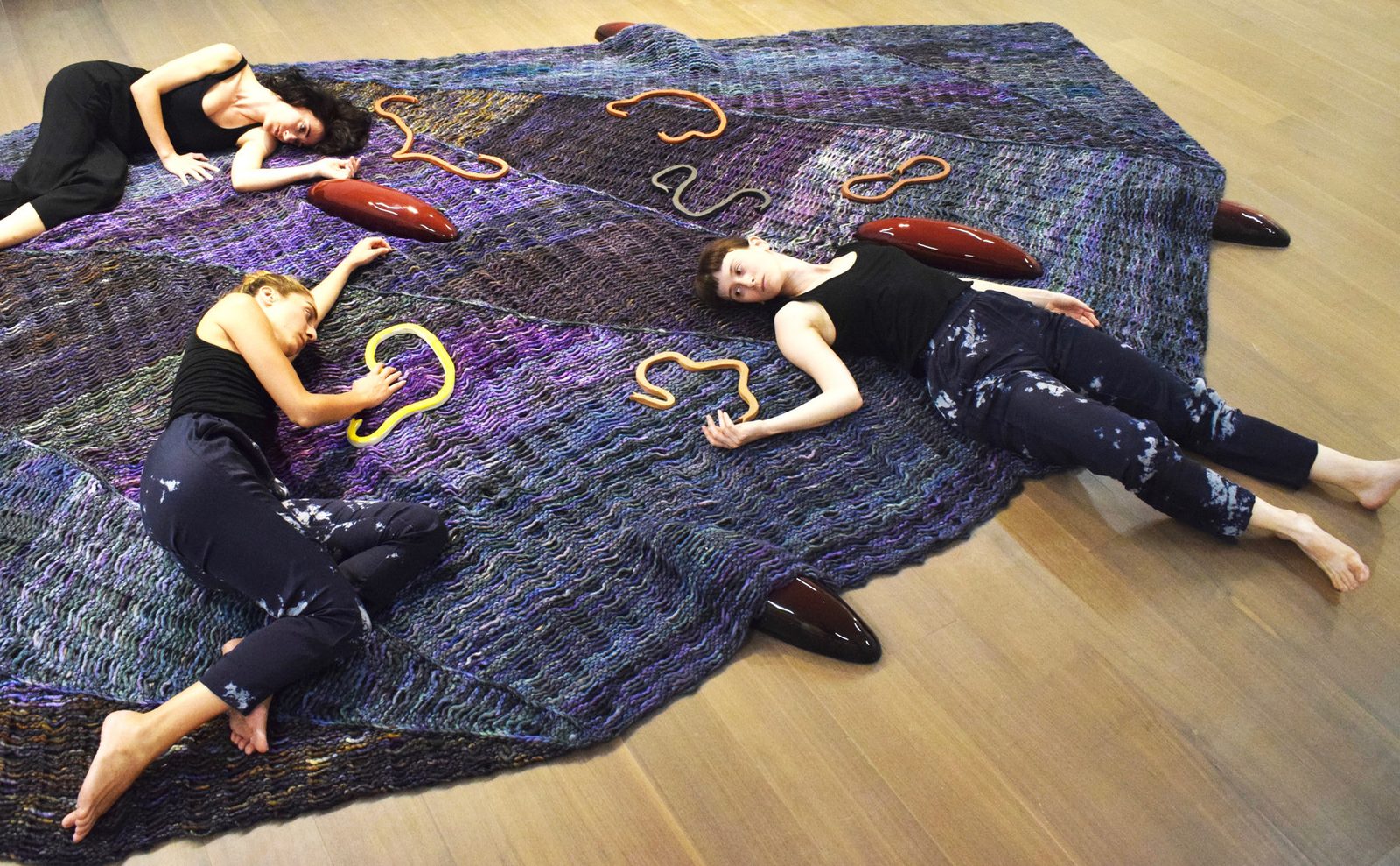 Three performers lying on the knitted carpet