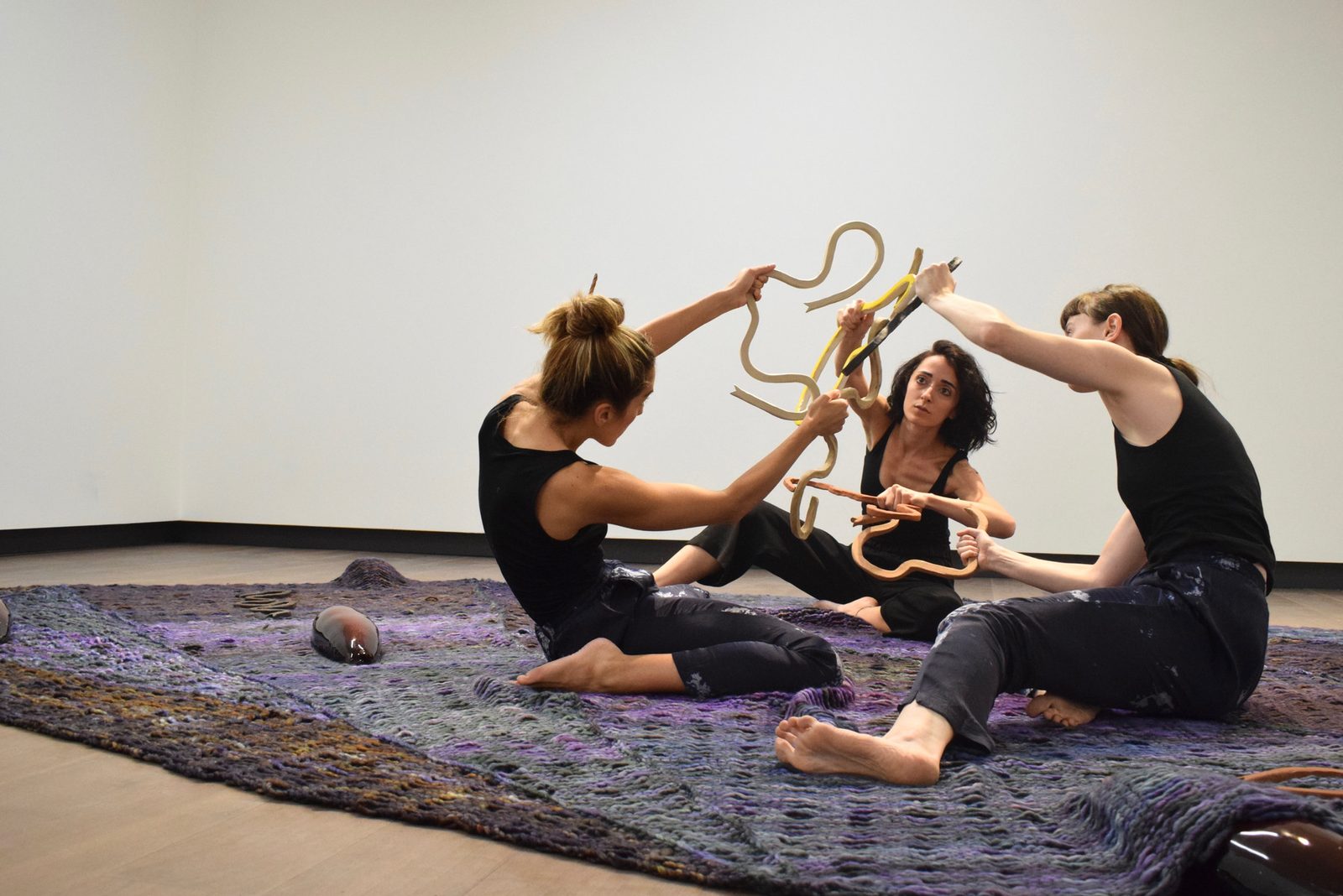 Three performers seated on the carpet lifting a rope form together