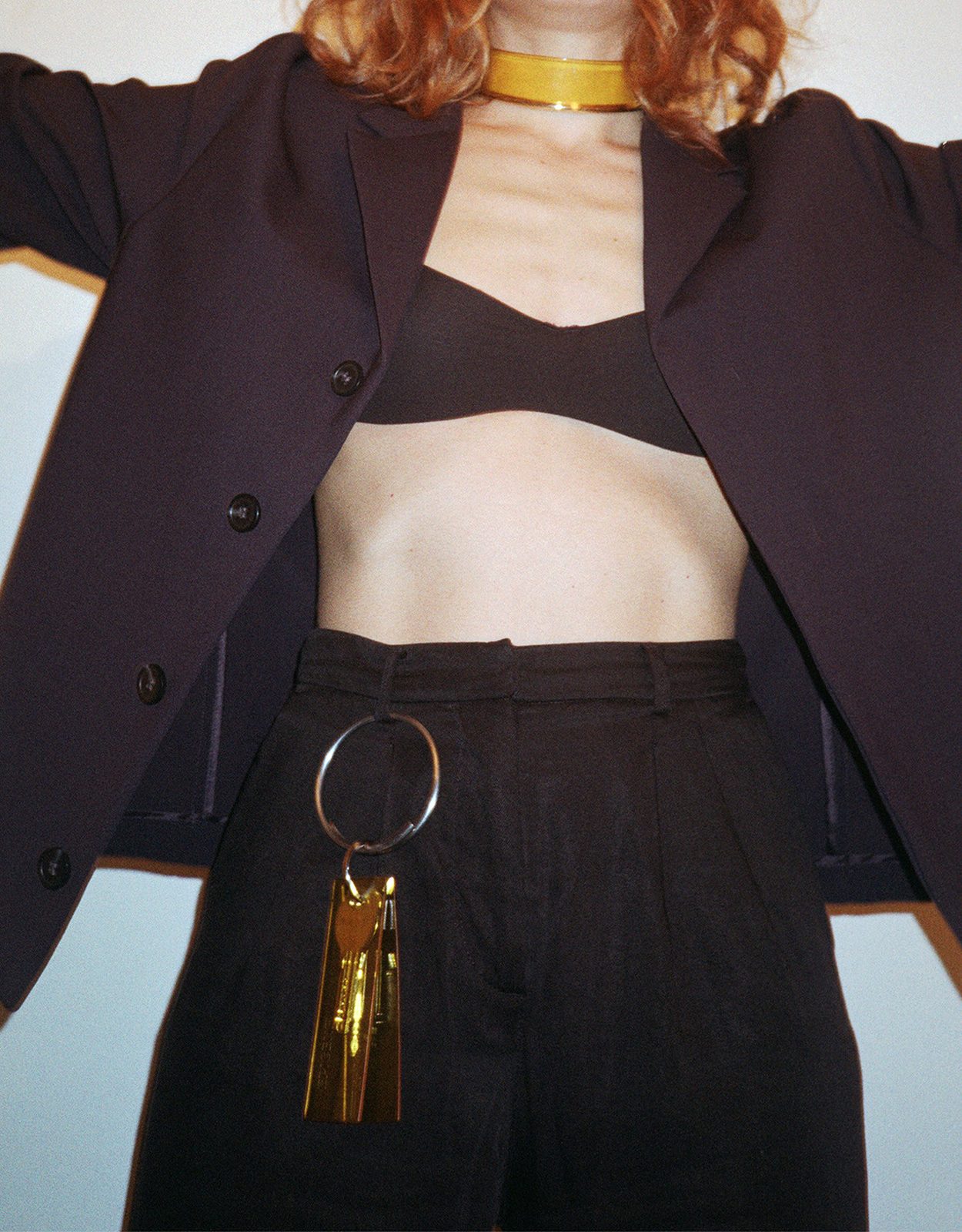 A model in a dark jacket with a yellow choker and a metal ring at her waist
