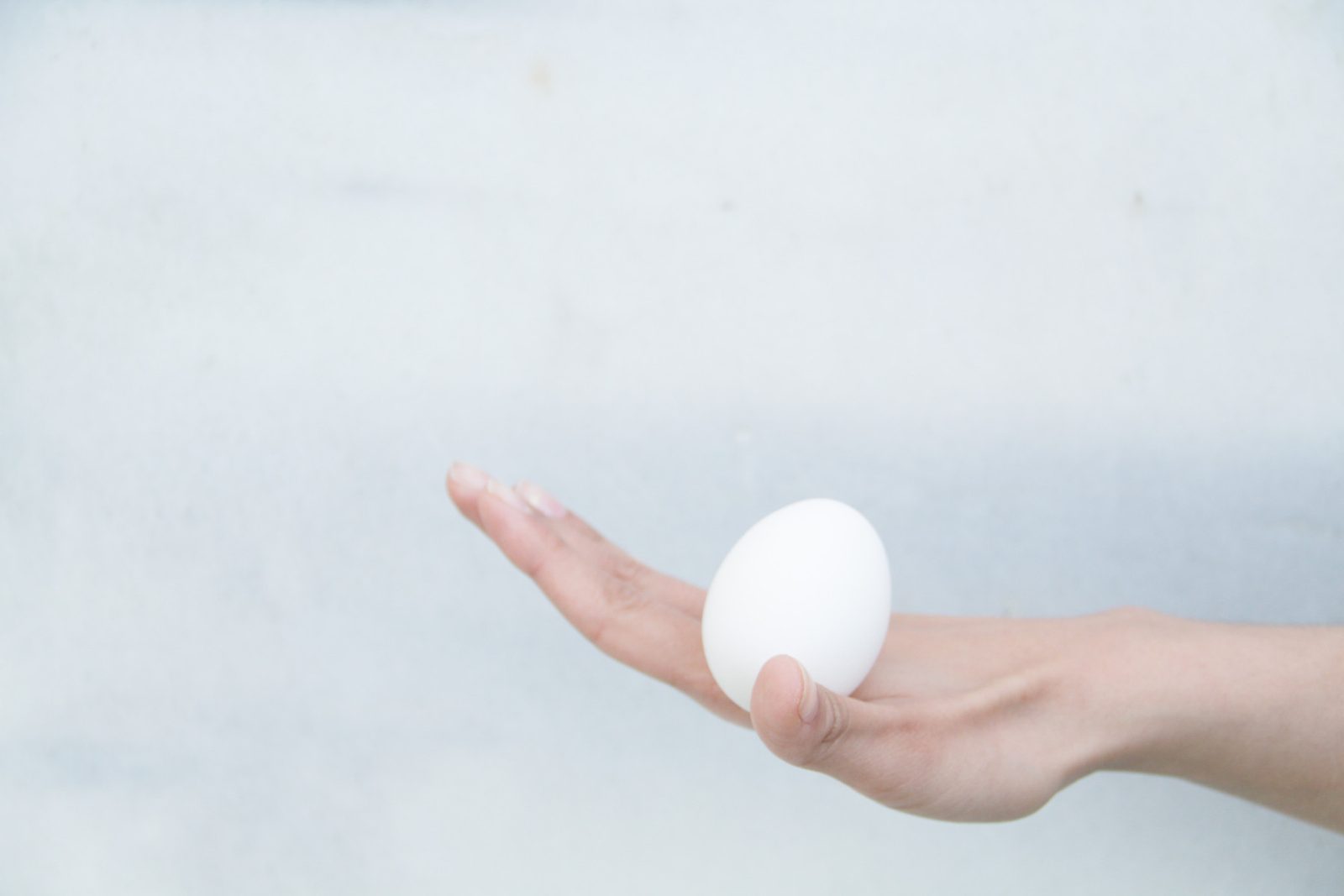 An egg balanced on an open palm against a pale wall