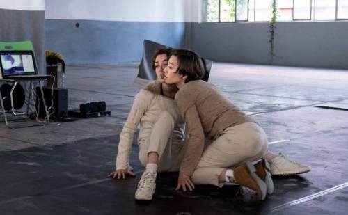 Two performers mirroring each other on all fours in front of tall windows