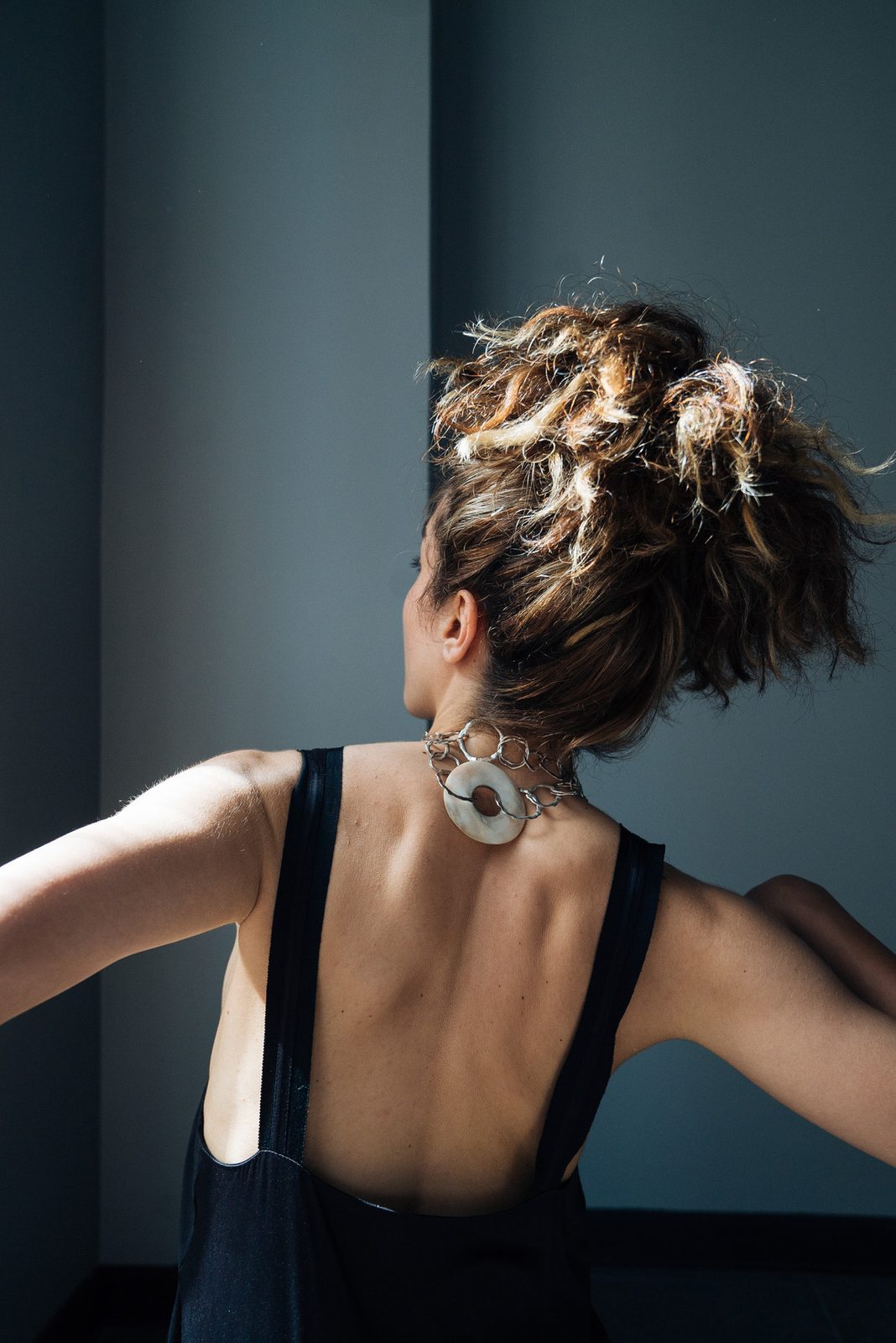 Dila from behind in a black dress, a pendant at the nape of her neck