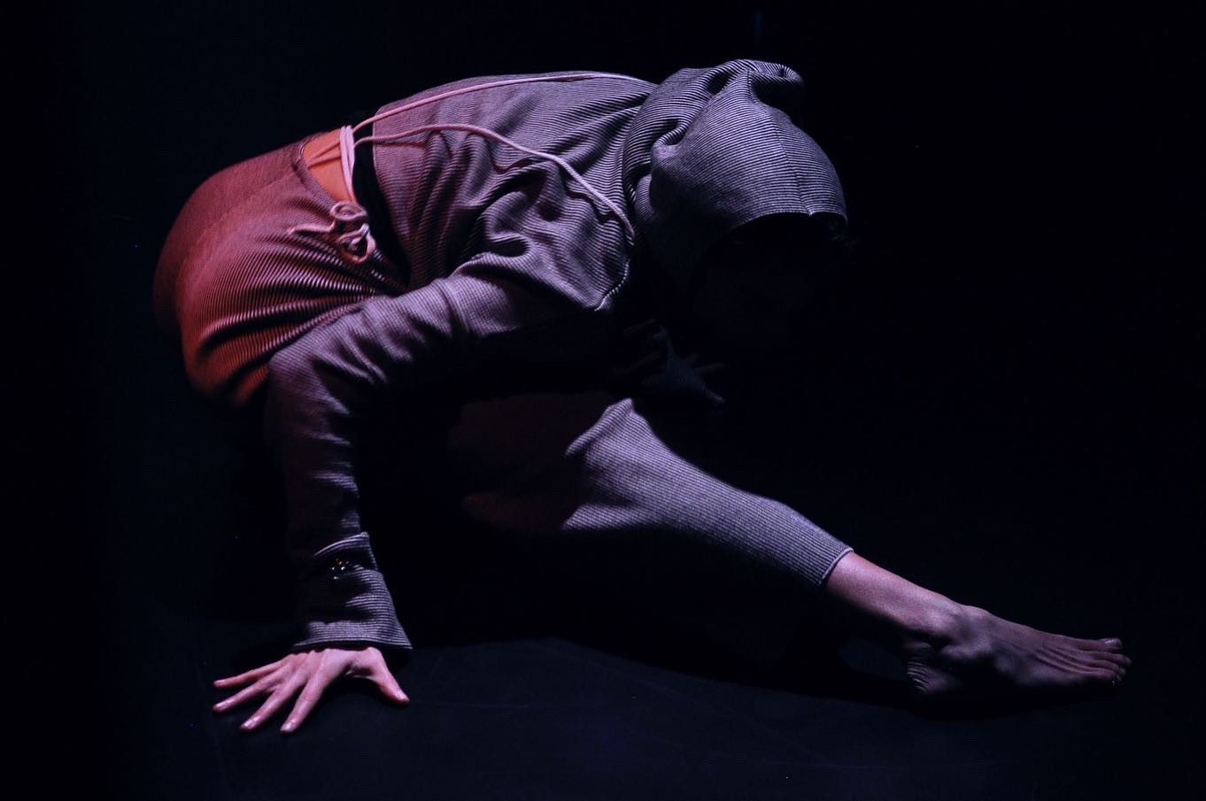 A crouched figure in a hooded top under dim red light