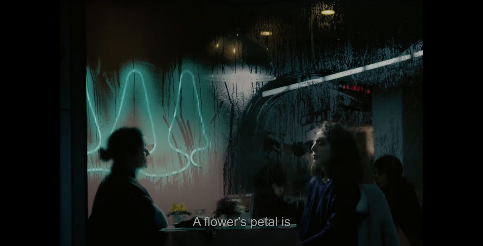 Two women talking in a dim cafe, neon light reflected in the window, still from the film